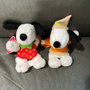 Two stuffed snoopy animals in strawberry and scarecrow outfit
